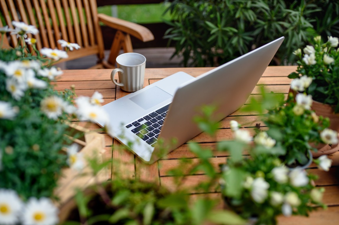 Fotografi av en bærbar pc på et bord som står i en hage utendørs, med en kaffekopp